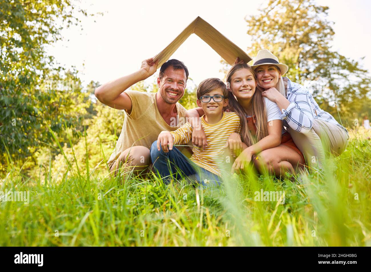 Famiglia felice in un prato con un tetto sopra le loro teste come simbolo di proprietà domestica Foto Stock