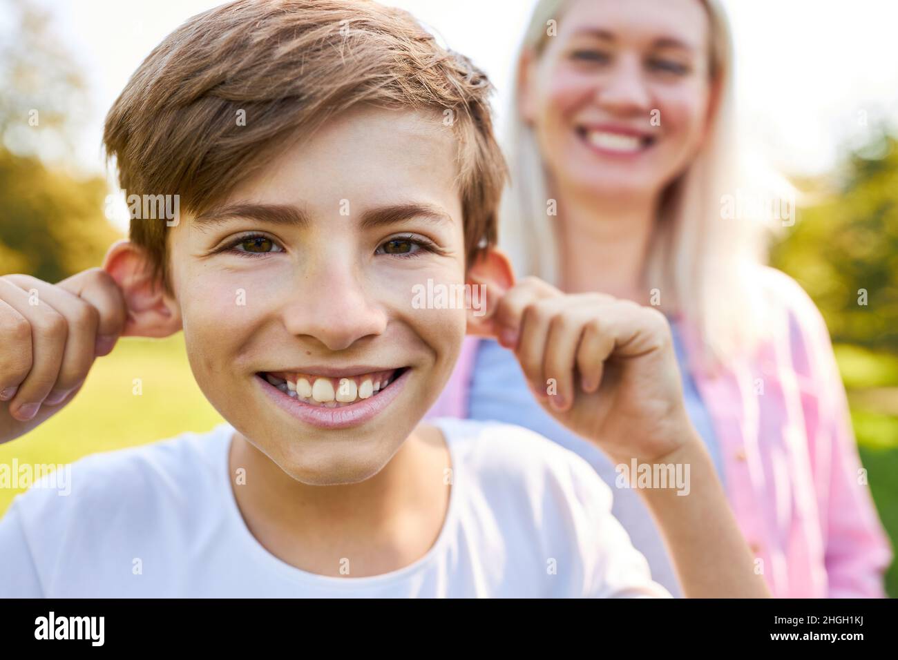 Ragazzo felice che volava tirare le orecchie con la madre sullo sfondo Foto Stock
