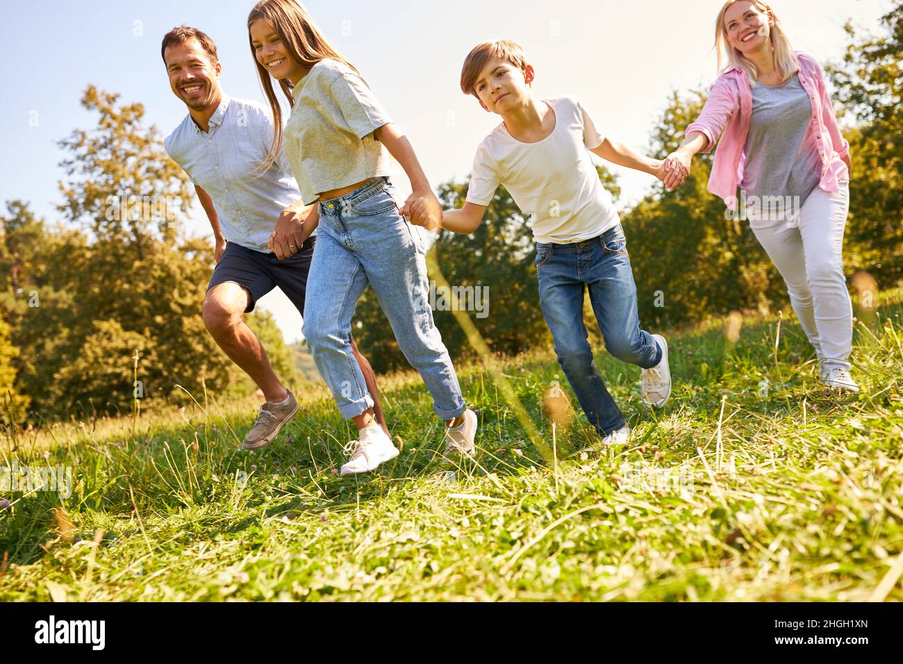 I genitori e due bambini camminano di mano in mano su un prato verde in natura Foto Stock