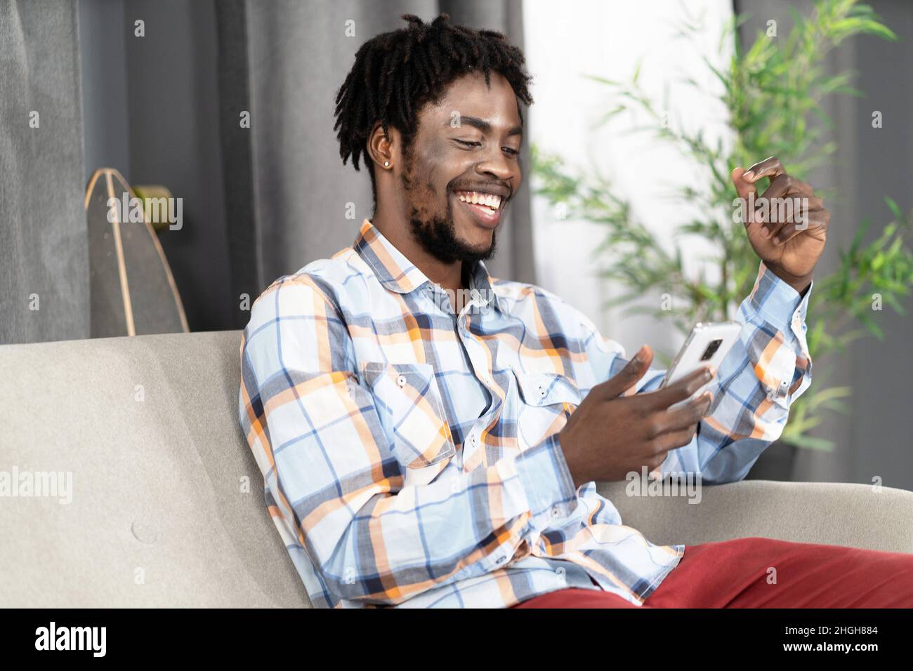 Uomo positivo in abiti casual seduto nel divano e guardando Fenny Memes sul suo smartphone. Divertente Dude Laughing e guardando sullo schermo del suo dispositivo mobile sul divano. Primo piano. Foto di alta qualità Foto Stock