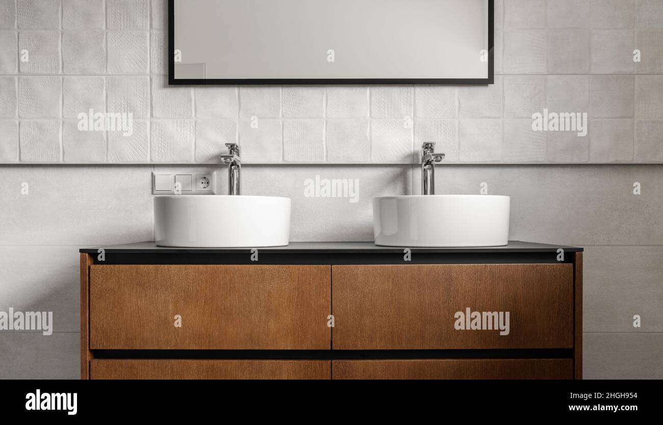 Bagno moderno vanity unita' con due lavandini rotondi in ceramica, rubinetti cromati e specchio con cornice nera, racconti bianchi e armadietto in legno. Bar contemporaneo Foto Stock