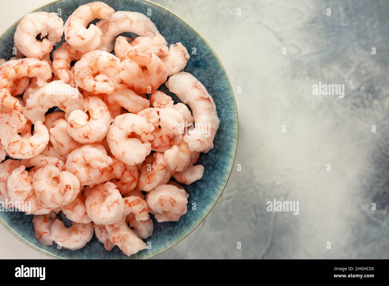 Primo piano i gamberetti surgelati con cubetti di ghiaccio su un piatto blu su sfondo blu sfocato con spazio per la copia. Gamberi che cucinano. Alimenti congelati. Mediterranea Foto Stock