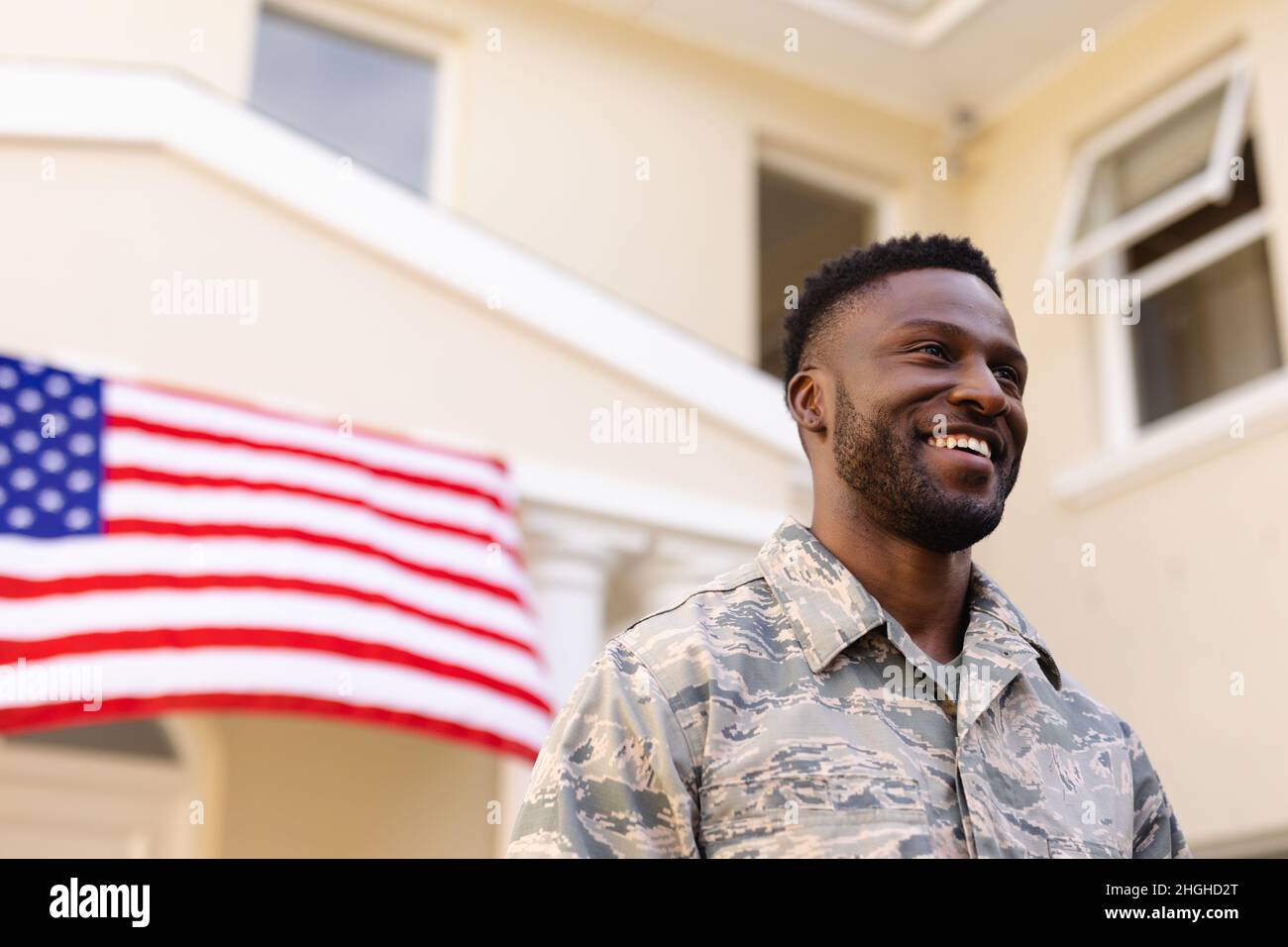 Sorridente uomo dell'esercito afroamericano che guarda via contro casa con bandiera americana Foto Stock