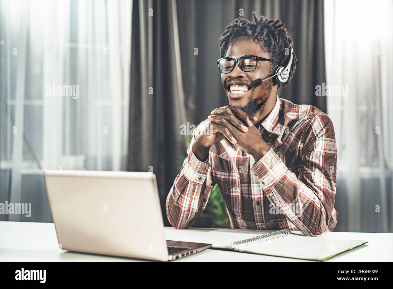 Il giovane insegnante di lingua inglese sta dando la video lezione in linea. Piano del semestre di studio. L'uomo si siede al tavolo e guarda lo schermo del laptop in cuffie con microfono. Primo piano. Foto di alta qualità Foto Stock