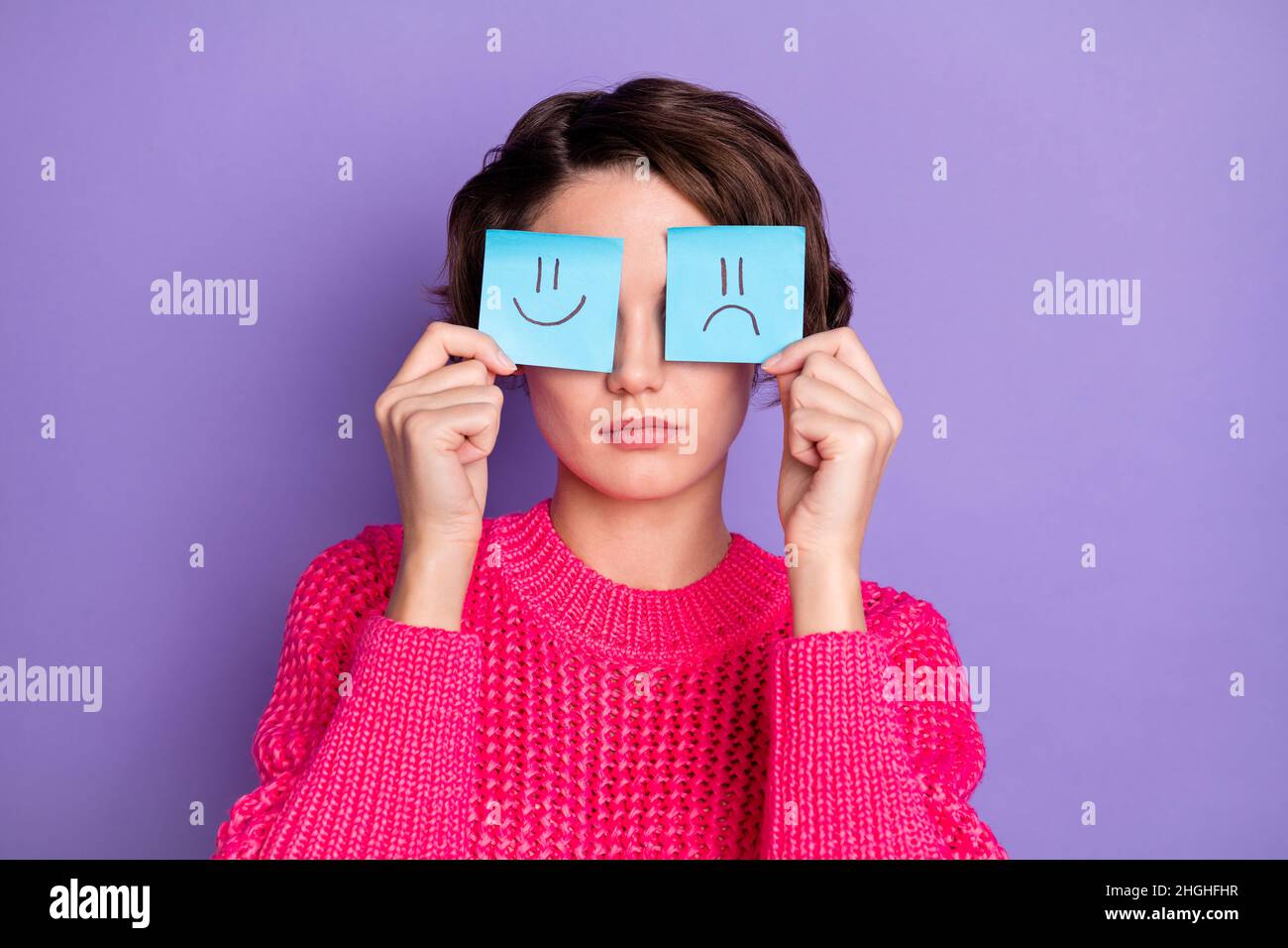 Foto di bello hairdo giovane persona braccia tenendo carta emoji carte che coprono gli occhi isolati su sfondo di colore violetto Foto Stock