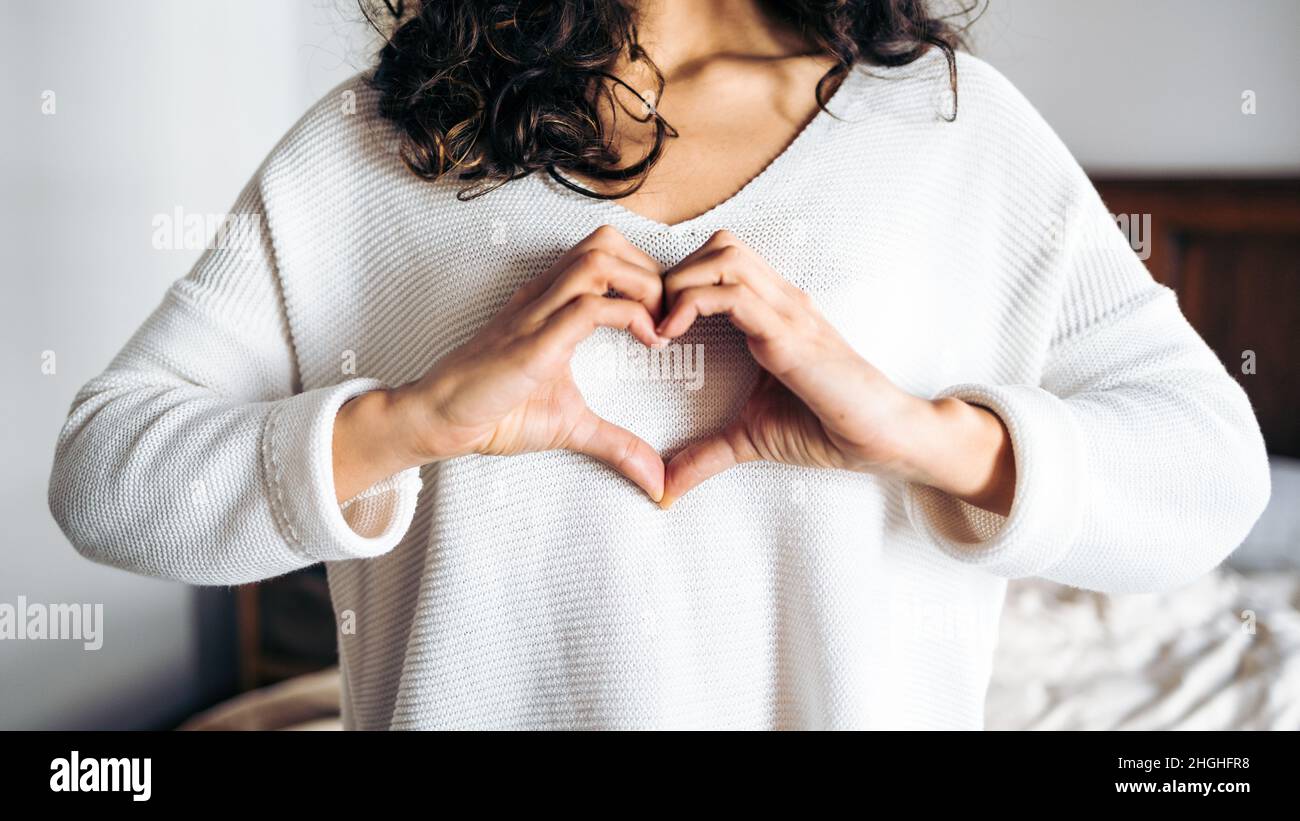 Giovane donna irriconoscibile che fa gesto d'amore. Le mani che formano una forma carina del cuore. Foto Stock