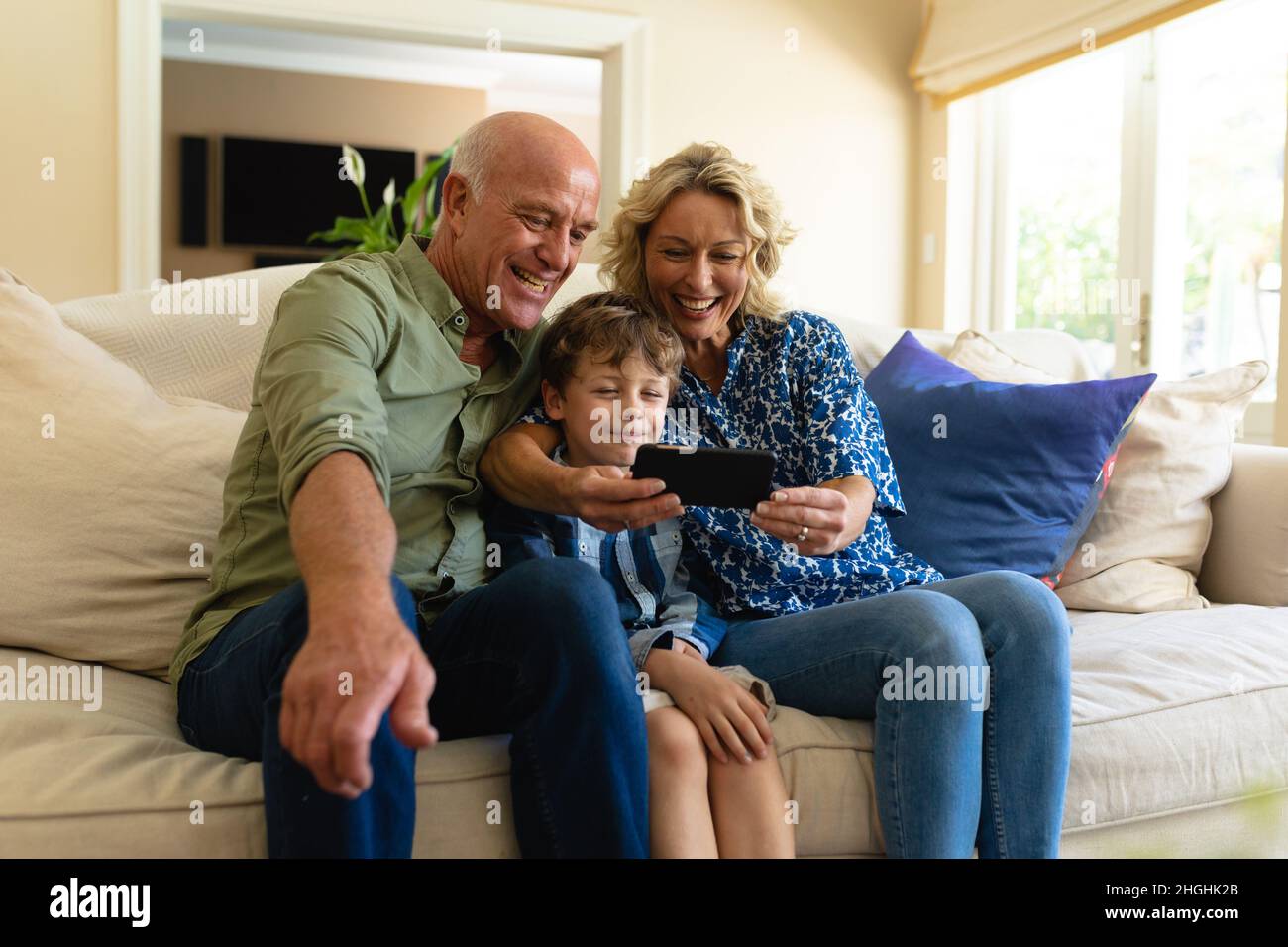 Nonni caucasici e nipote che usano un tablet digitale mentre si siedono sul divano di casa Foto Stock