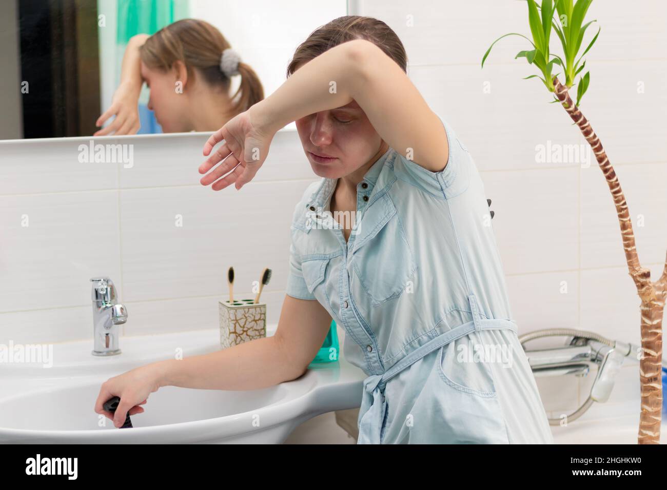 Una giovane donna pulitore in un bagno luminoso con uno stantuffo per eliminare il blocco nelle sue mani. Sul muro c'è uno specchio con un riflesso. Pianta verde. Foto Stock