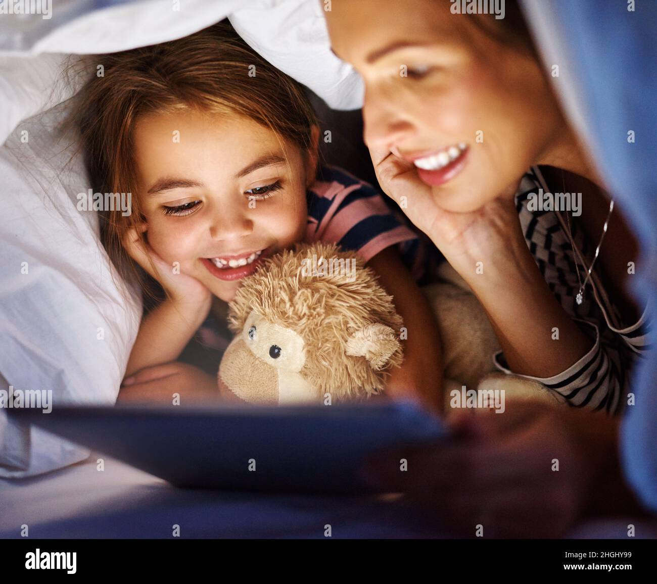 La moderna storia della notte. Scatto corto di una giovane donna incinta attraente che legge sua figlia una storia di doratura su un tablet. Foto Stock