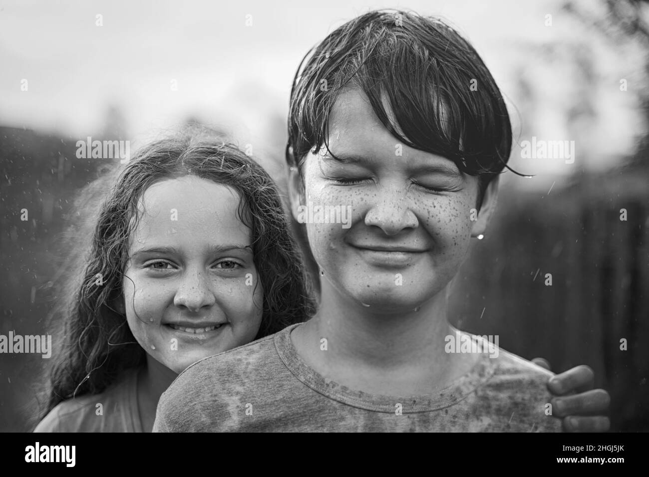 I bambini carini si impachiscono e giocano nel ritratto di famiglia in bianco e nero, sotto la pioggia. Amicizia o mondo abbraccio giorno concetto. Foto Stock