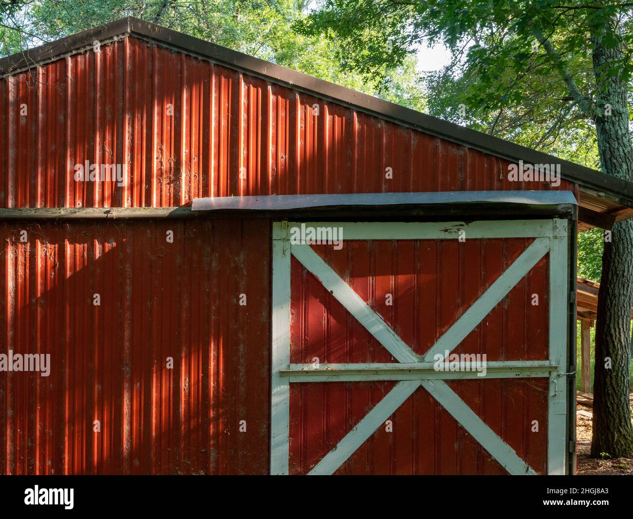 Capannone rosso in azienda ha una porta scorrevole con rivestimento bianco. La luce del sole rivela la presenza di teli di ciottoli polverosi sulla parete. Foto Stock