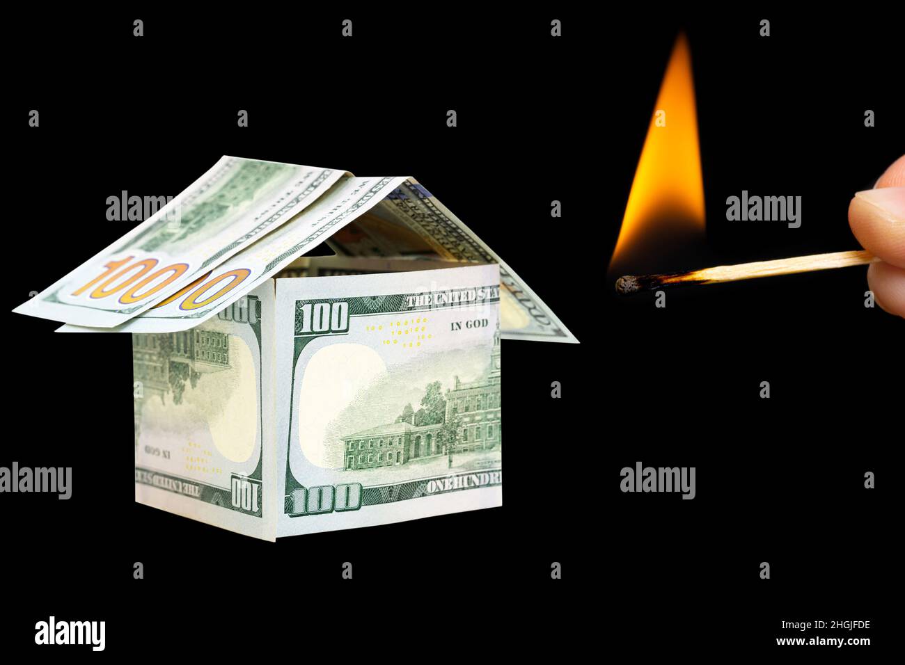 Mano che tiene una partita bruciante vicino ad una casa fatta dalle fatture del dollaro isolato su sfondo nero. Concetto di assicurazione antincendio. Foto Stock