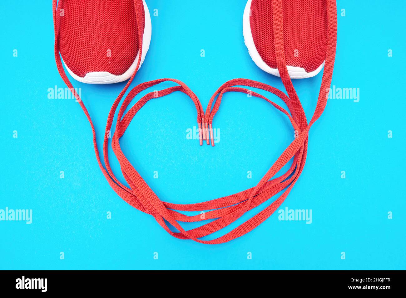 Simbolo del cuore realizzato dalle scarpe delle sneaker atletiche rosse su sfondo blu. Innamorati del concetto di corsa. Foto Stock