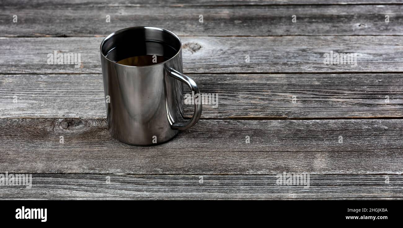 Caffè scuro all'interno di una tazza in acciaio inox su un tavolo in legno invecchiato con spazio per la copia Foto Stock