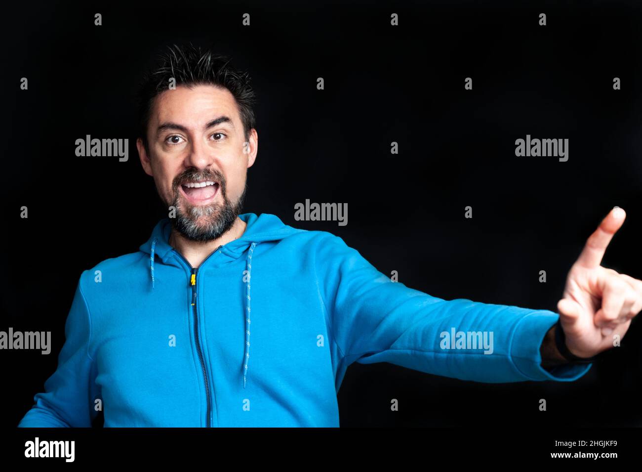Giovane adulto con barba e capelli spiky vestito con una felpa blu, guardando direttamente nella fotocamera con la bocca aperta esprimendo gioia e felicità Foto Stock