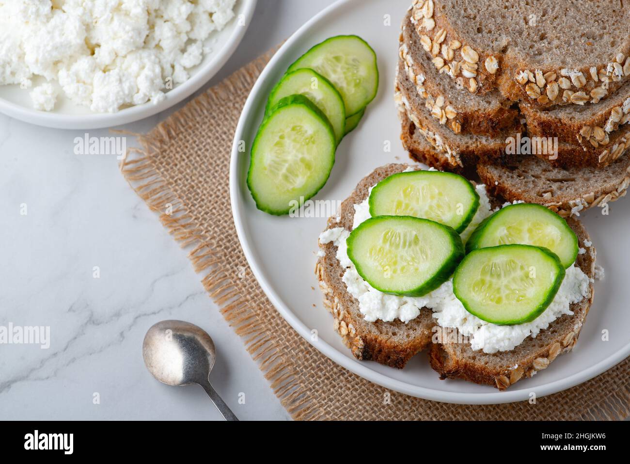 Fette di pane di segale con formaggio casereccio e cetrioli su sfondo bianco. Foto Stock