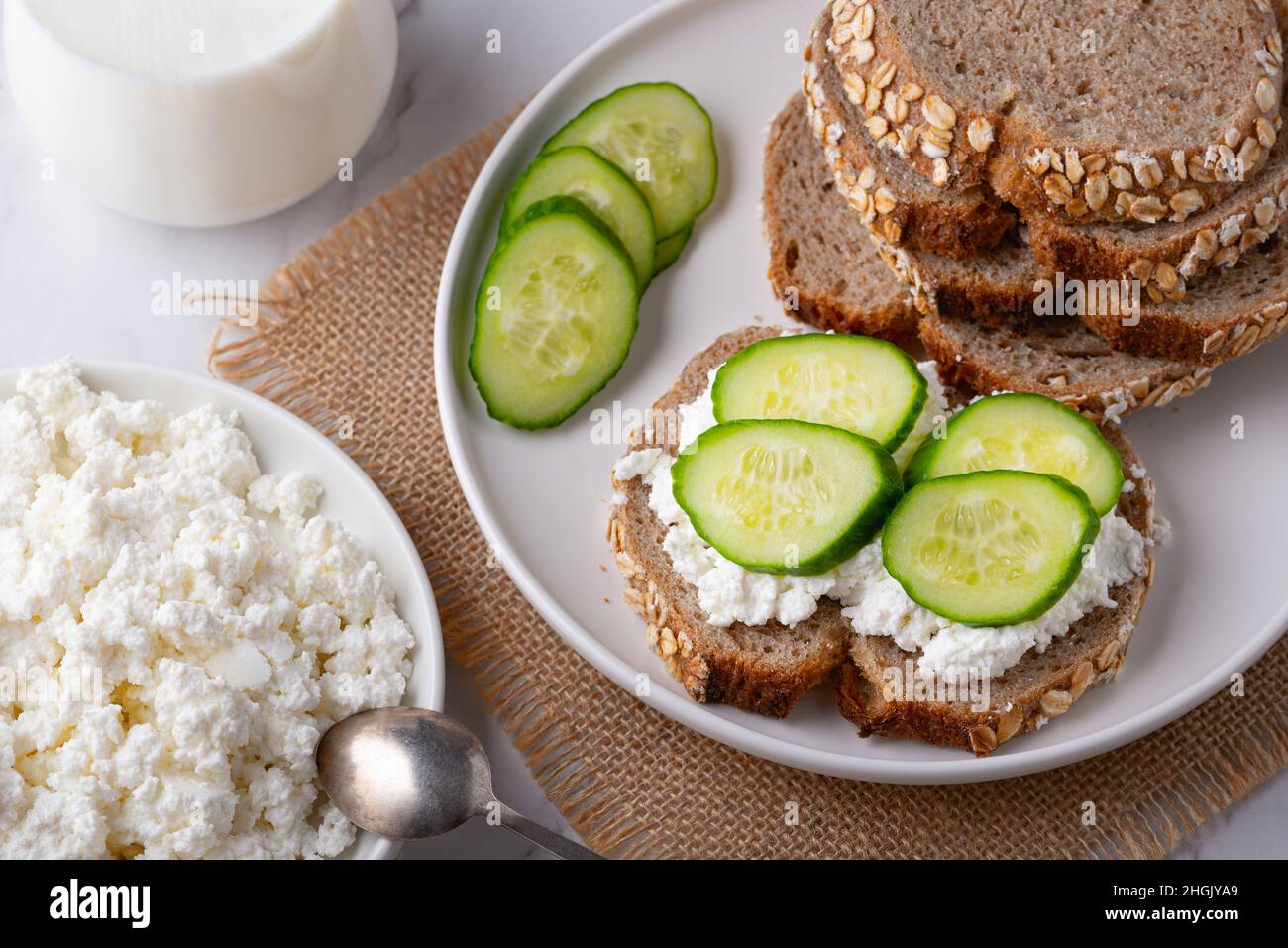 Fette di pane di segale con formaggio casereccio e cetrioli su sfondo bianco. Foto Stock