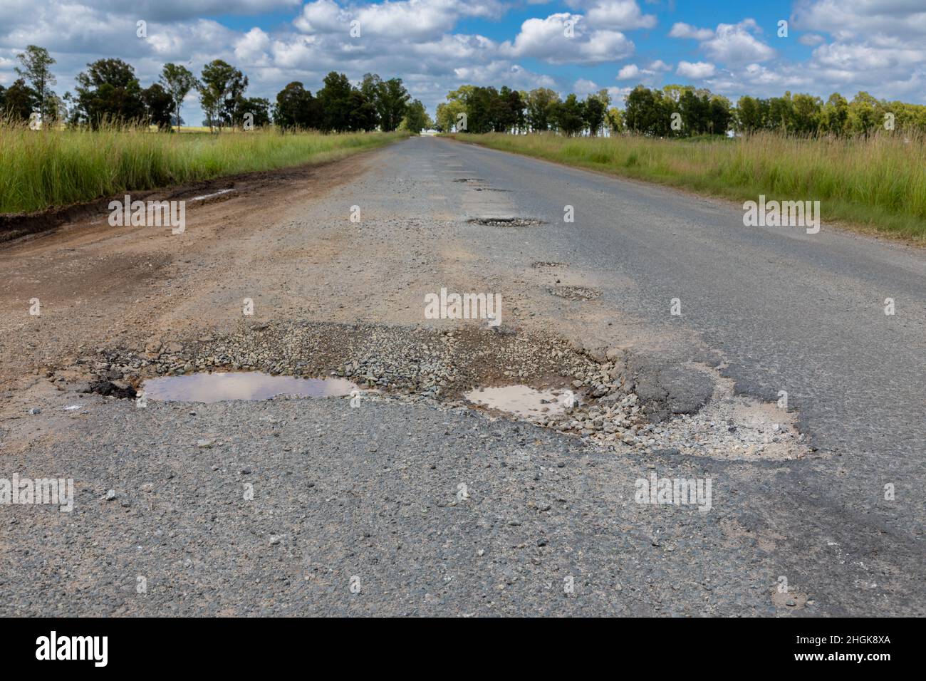 Strada asfaltata con una pothole molto grande e profonda. Il POTHOLE è riempito per metà con acqua. Foto Stock