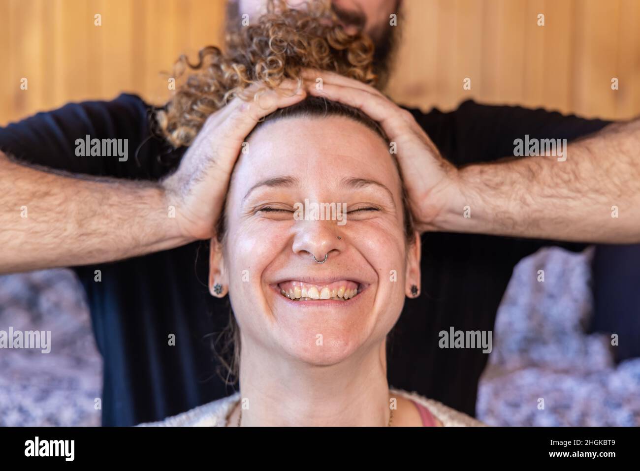 Una felice donna caucasica agli inizi degli anni trenta, è vista con un ampio sorriso come un praticante Shiatsu massaggia la testa con spazio per la copia su entrambi i lati. Foto Stock