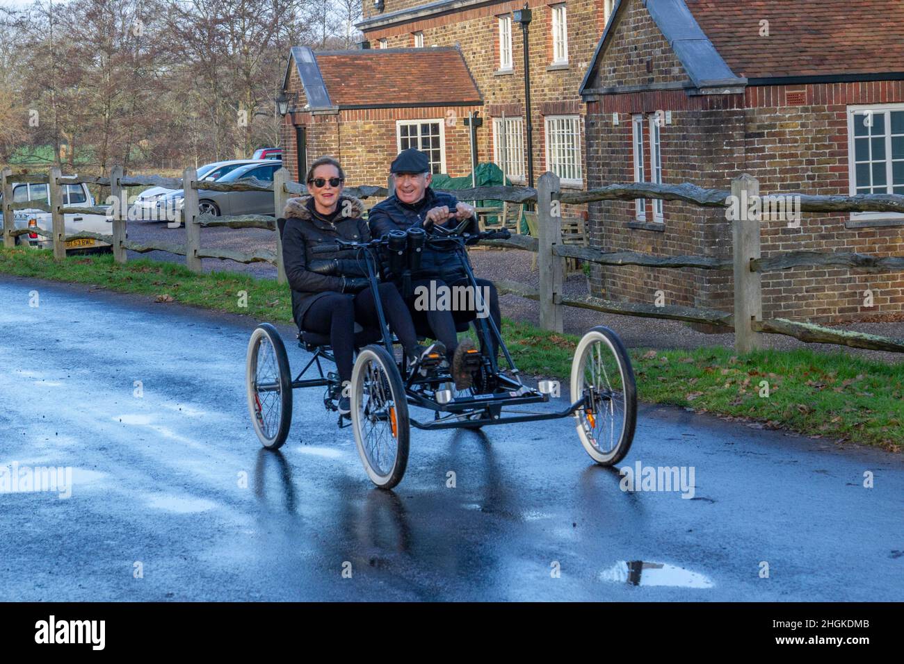 Uomo e donna su una bicicletta a due posti a quattro ruote che attraversa il villaggio a Windsor Great Park, Windsor, Berkshire, Regno Unito. Foto Stock
