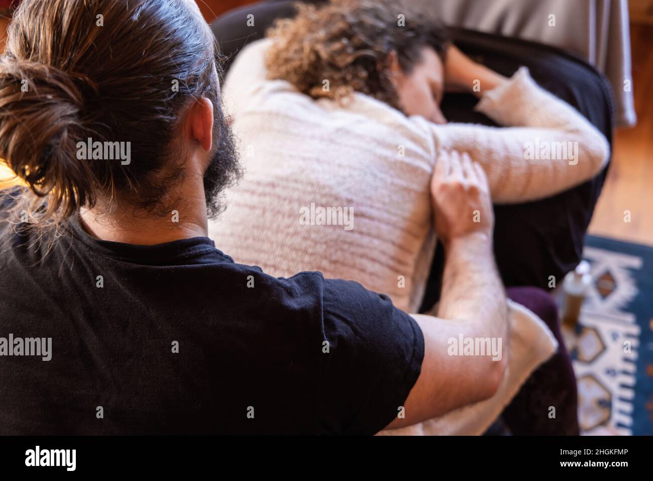 Un terapista di medicina alternativa è visto da vicino e da dietro in fuoco morbido, massaggiando le spalle di una donna rilassata con sfondo sfocato. Foto Stock