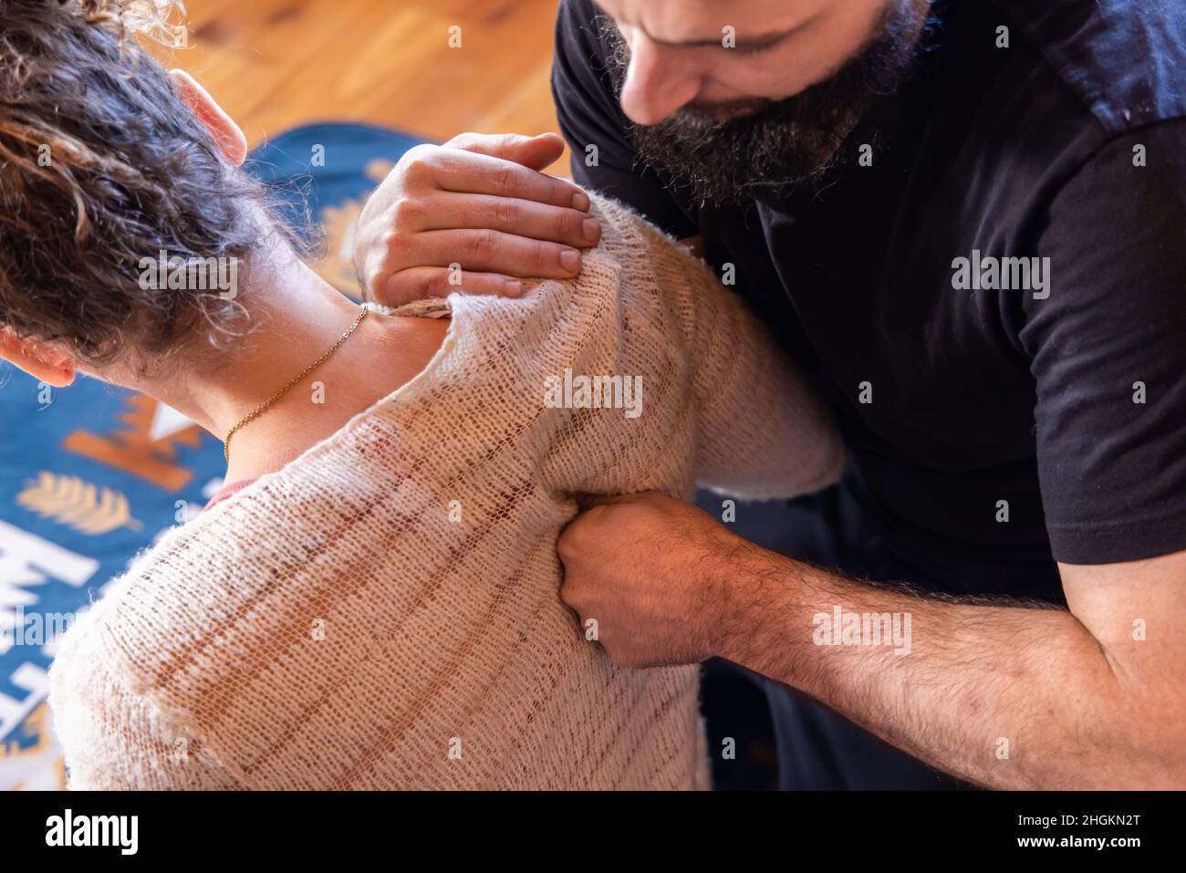 La vista del fuoco selettivo ad angolo alto come un terapeuta Shiatsu maschio è vista impastare la spalla di una donna, nella posizione seduta con lo spazio di copia a destra. Foto Stock