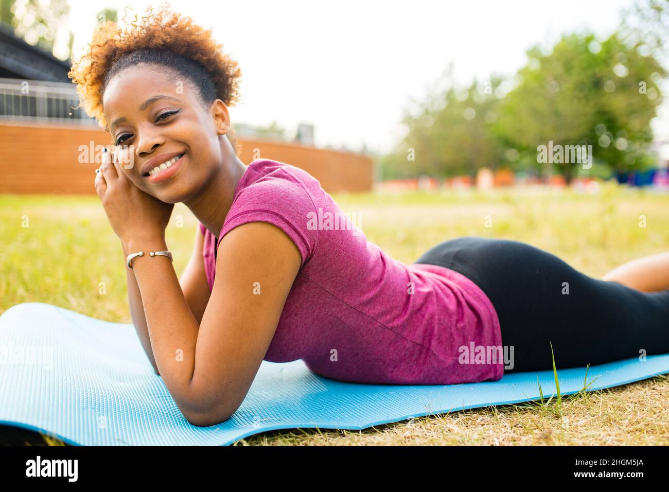 Giovane allenatore afro-americano felice con capelli ricci corti pronti per il tempo di yoga all'aperto Foto Stock