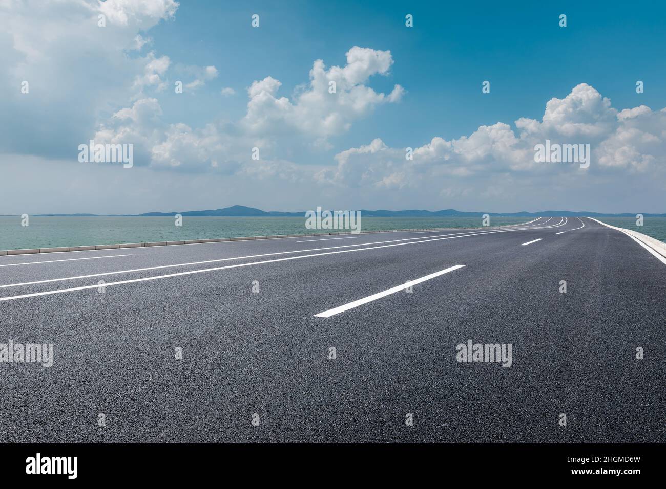 Strada asfaltata e fiume con montagne sotto il cielo blu Foto Stock