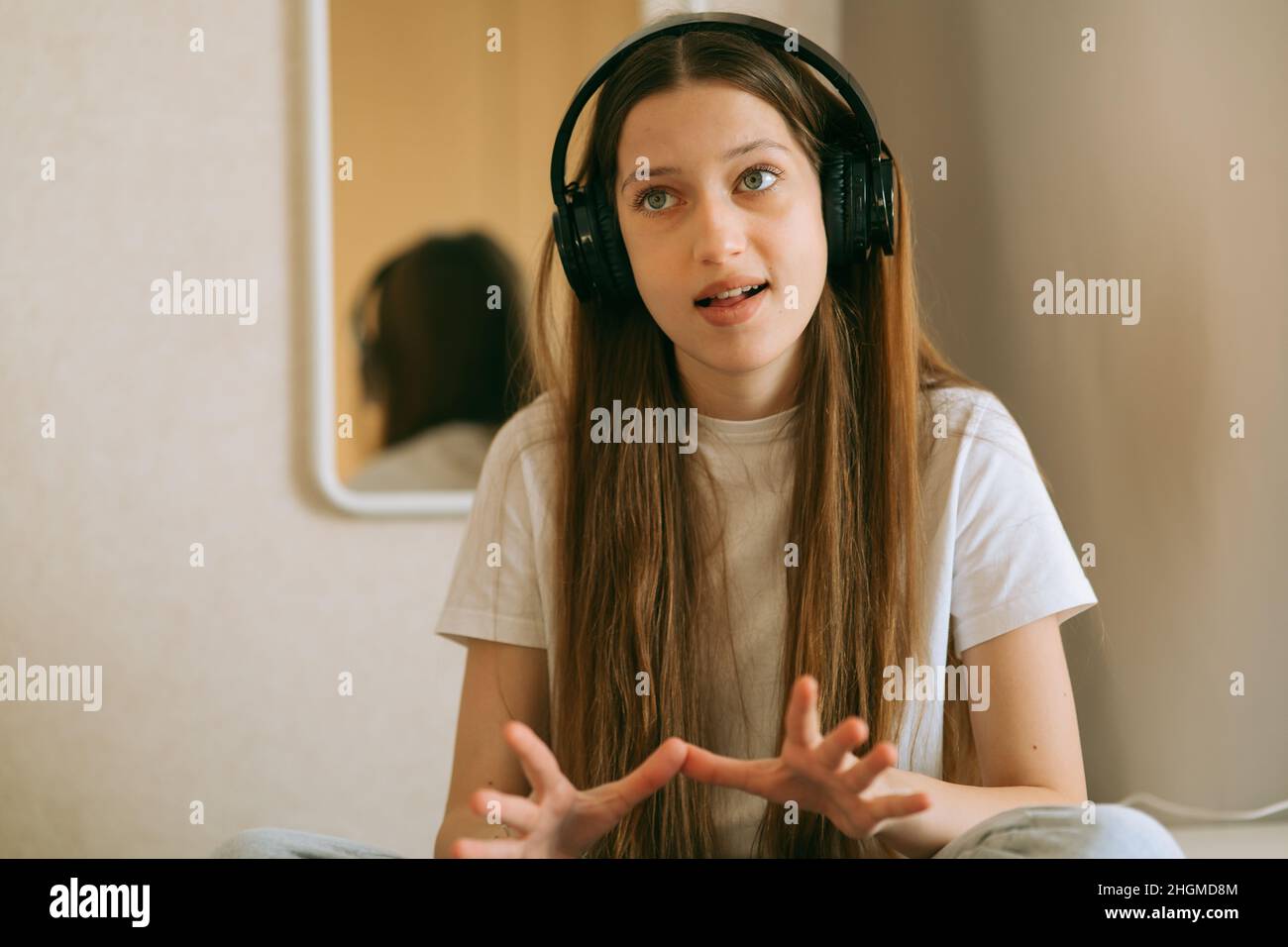 Una bella ragazza caucasica adolescente, generazione Z con capelli lunghi in cuffie, a casa ascolta le lezioni audio, treni pronuncia. Scuola domestica Foto Stock