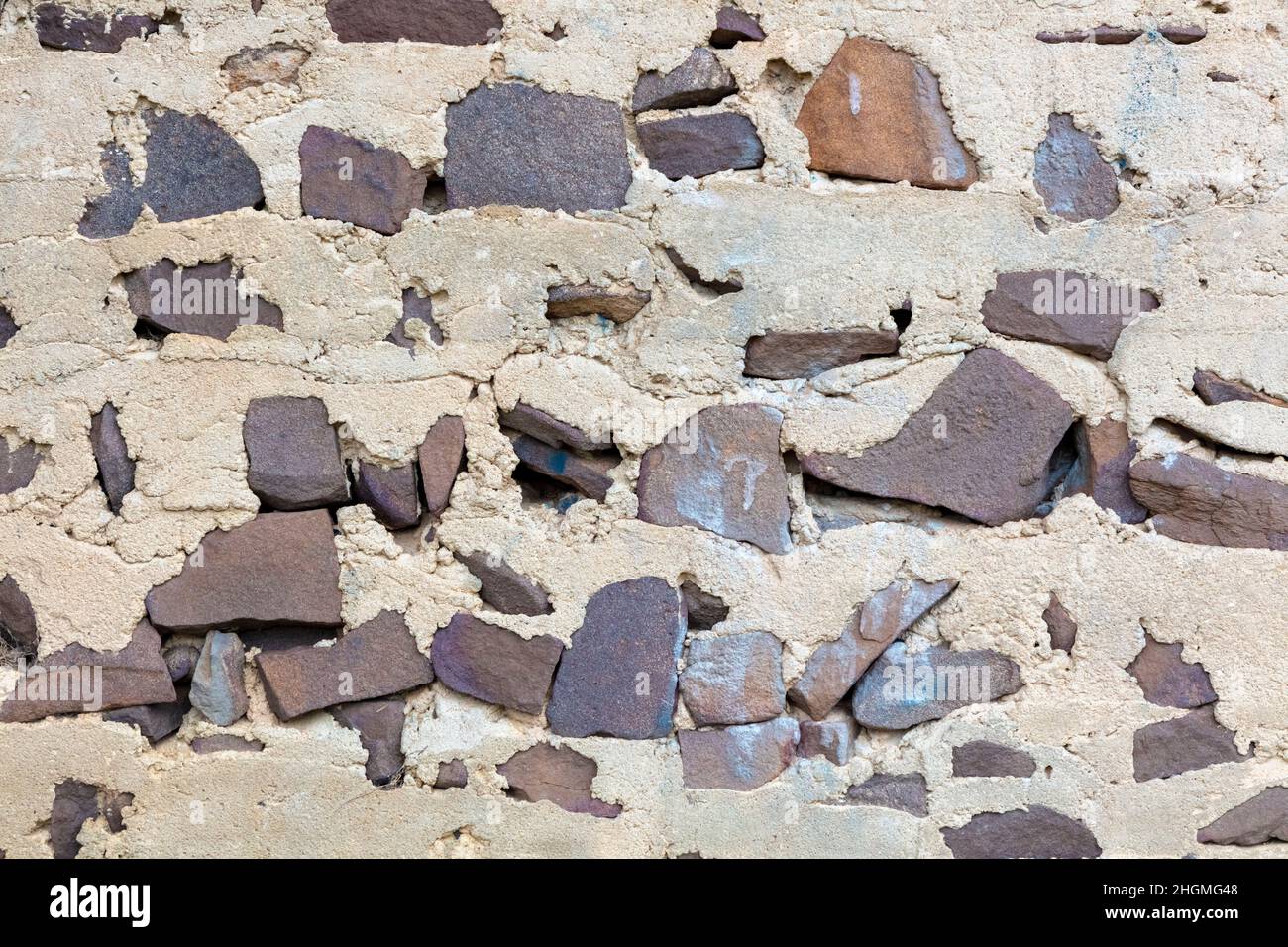 Fotografia di una vecchia e deteriorante parete fabbricata con calcestruzzo grigio che si sta rompendo e pietra di forma irregolare marrone Foto Stock