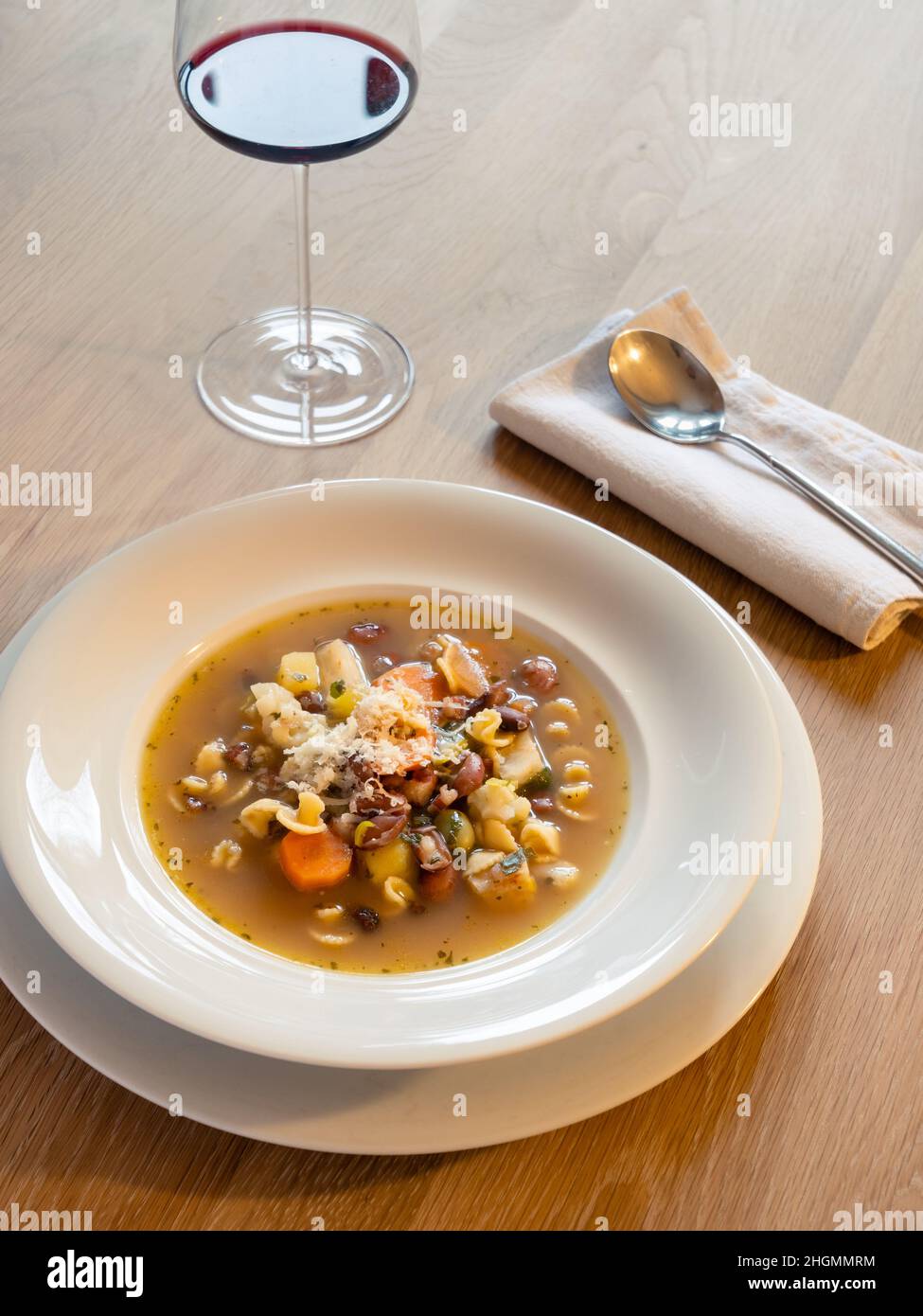 Minestrone zuppa di verdure italiane in un piatto bianco con cucchiaio e bicchiere di vino Foto Stock