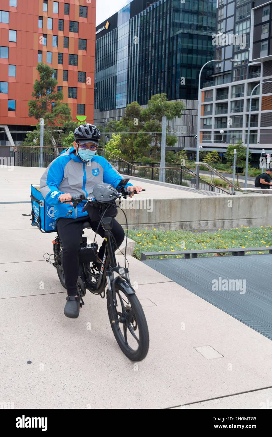 Un pilota di consegna su una bicicletta alimentata a batteria che indossa un casco e una maschera covid, corre sulla linea merci a Sydney, nuovo Galles del Sud, Australia Foto Stock