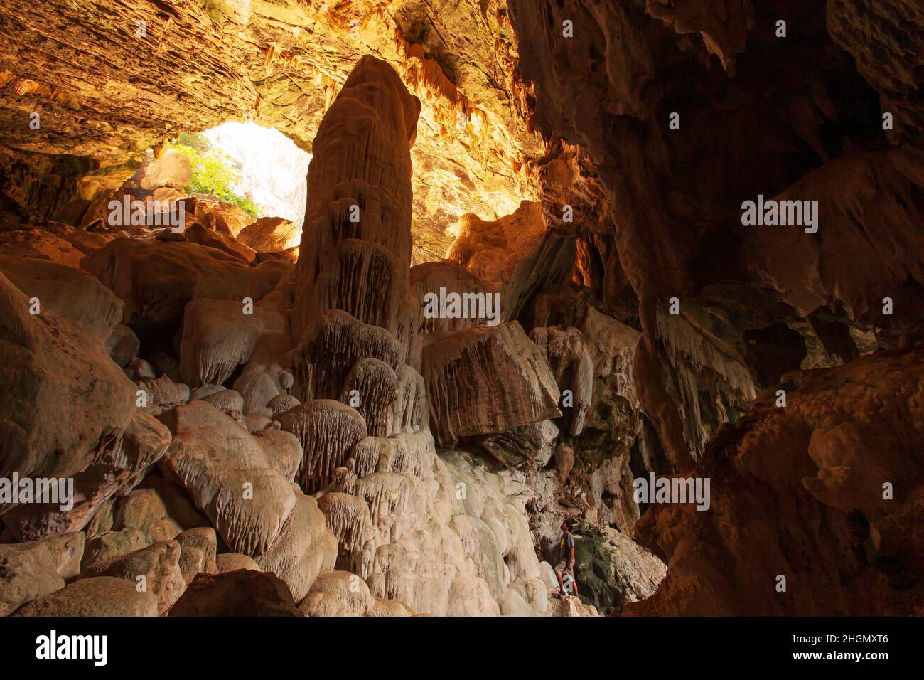 Un giovane asiatico in abbigliamento casual si alza e guarda la grande stalagmite nella grotta calcarea. Koh Wua Ta Lap Island, Thailandia. Foto Stock