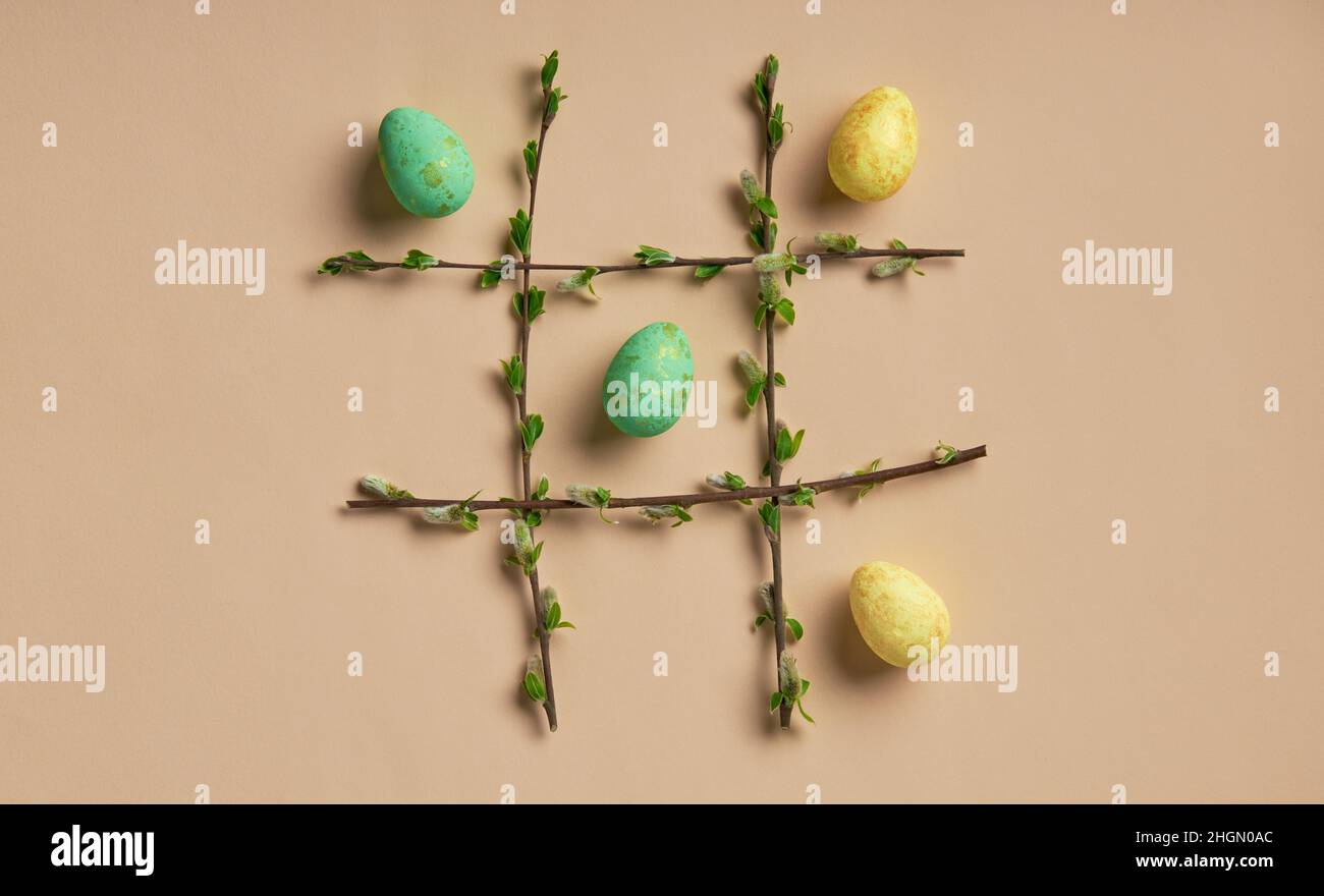 Uova di Pasqua in una cornice fatta di rametti primaverili su sfondo beige. Gioco TIC-tac-TOE. Tema pasquale flatlay. Foto Stock