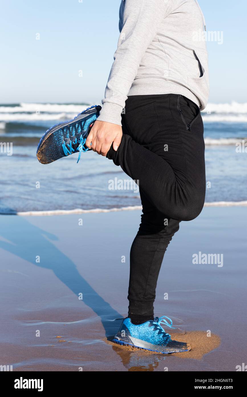 Uomo senza volto che stretching quadriceps muscolo al mare Foto Stock