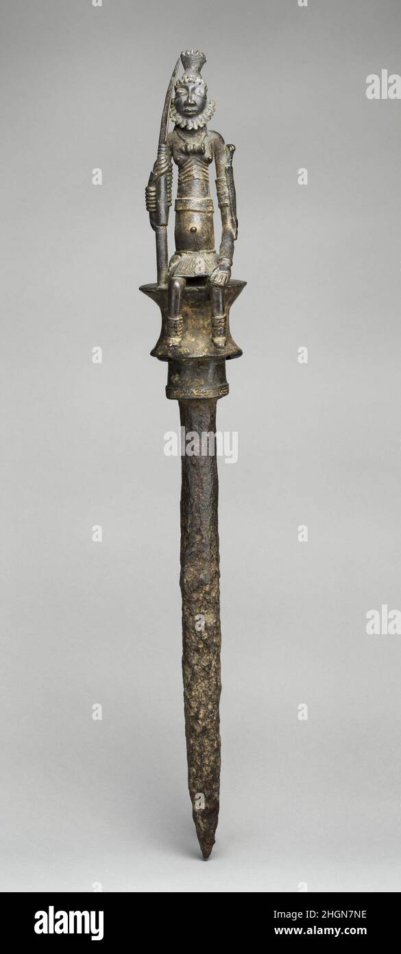 Staff: Uomini seduti Figura 16th–17th Century Dogon o Bozo popoli Una grande figura maschile in piena regalia, seduta su uno sgabello a forma di rocchetto, forma le finali di questo bastone di bronzo e ferro. Dettagli di vestito e ornamento del corpo-compreso il headdress elaborato e la barba stilizzata, motivi complessi sulla pelle, pendente pesante, armlets, braccialetti e caviglie, e gli involucri decorati intorno al petto e alla vita rivelano un individuo di alto stato. La figura tiene una lancia nella sua mano destra e porta un pugnale in una guaina decorata sul suo braccio sinistro, trasmettendo l'impressione di successo nella caccia come w Foto Stock