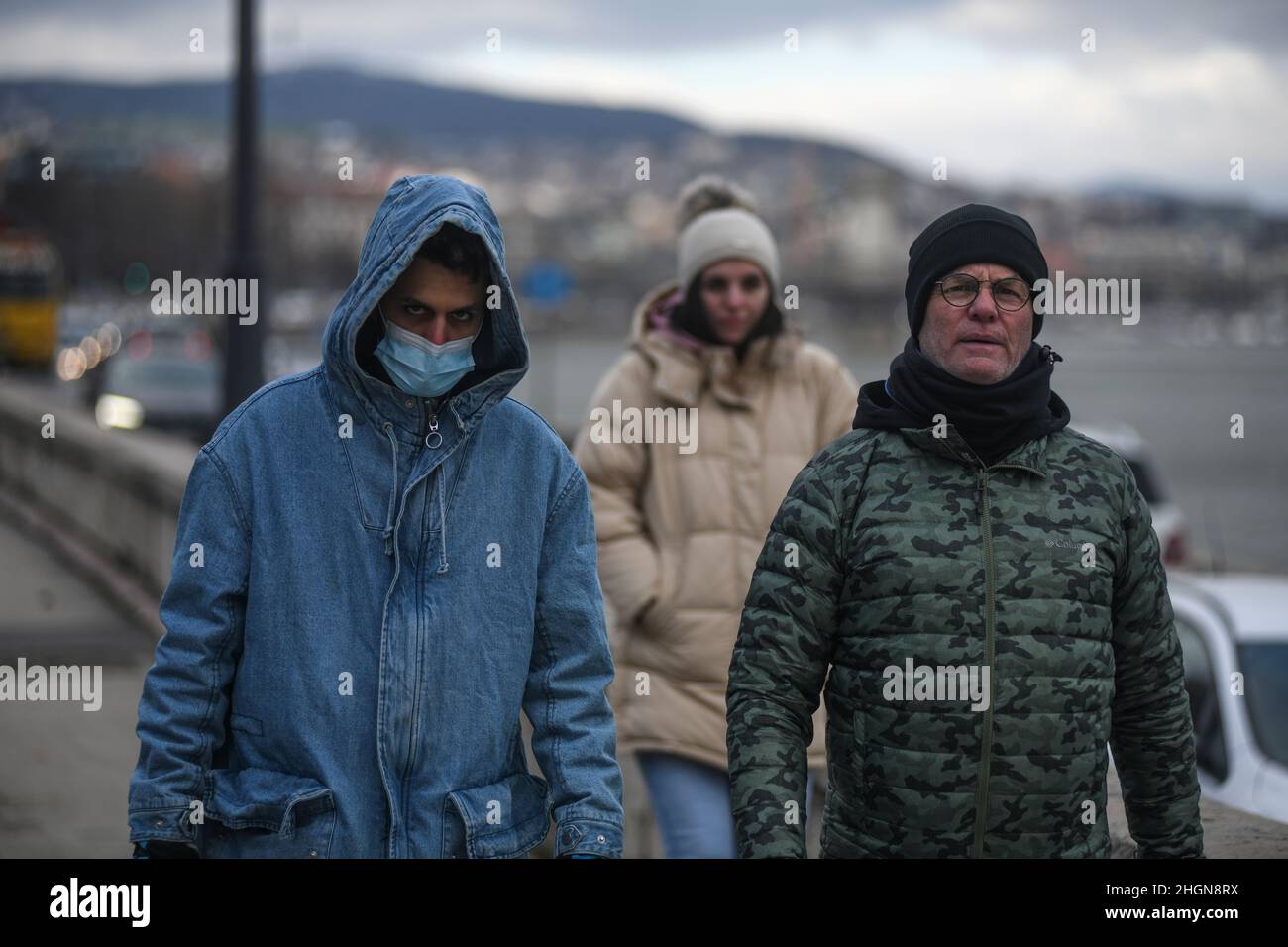 Persone che indossano maschere per il viso e abiti invernali sulla riva del Danubio, Budapest, Ungheria Foto Stock