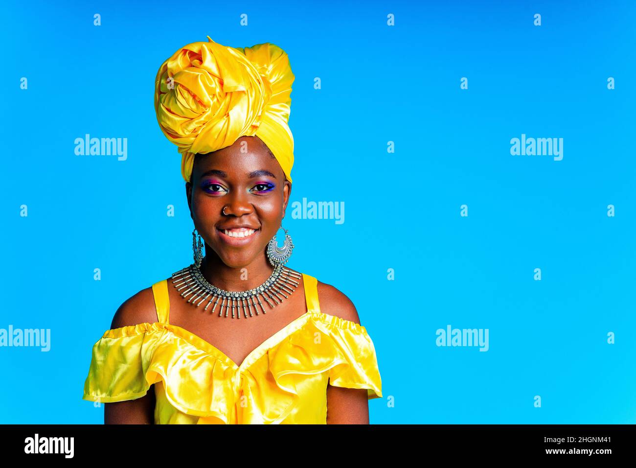 Donna africana con turbante di seta gialla e orecchini in argento e piercing al naso in blu studio sfondo Foto Stock