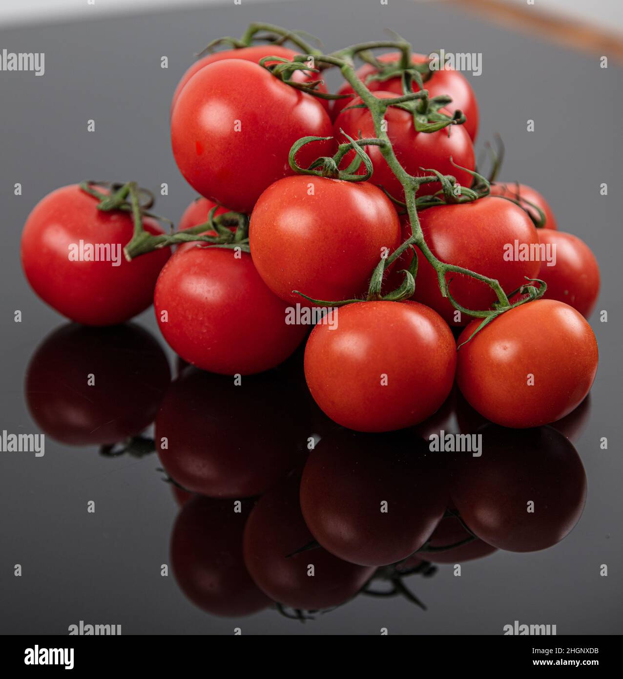 Bei pomodori freschi di vite (ciliegia) con gocce d'acqua, crudi, interi e dimezzati. Su sfondo nero con ardesia testurizzata. Ingredienti della Mediterranea Foto Stock