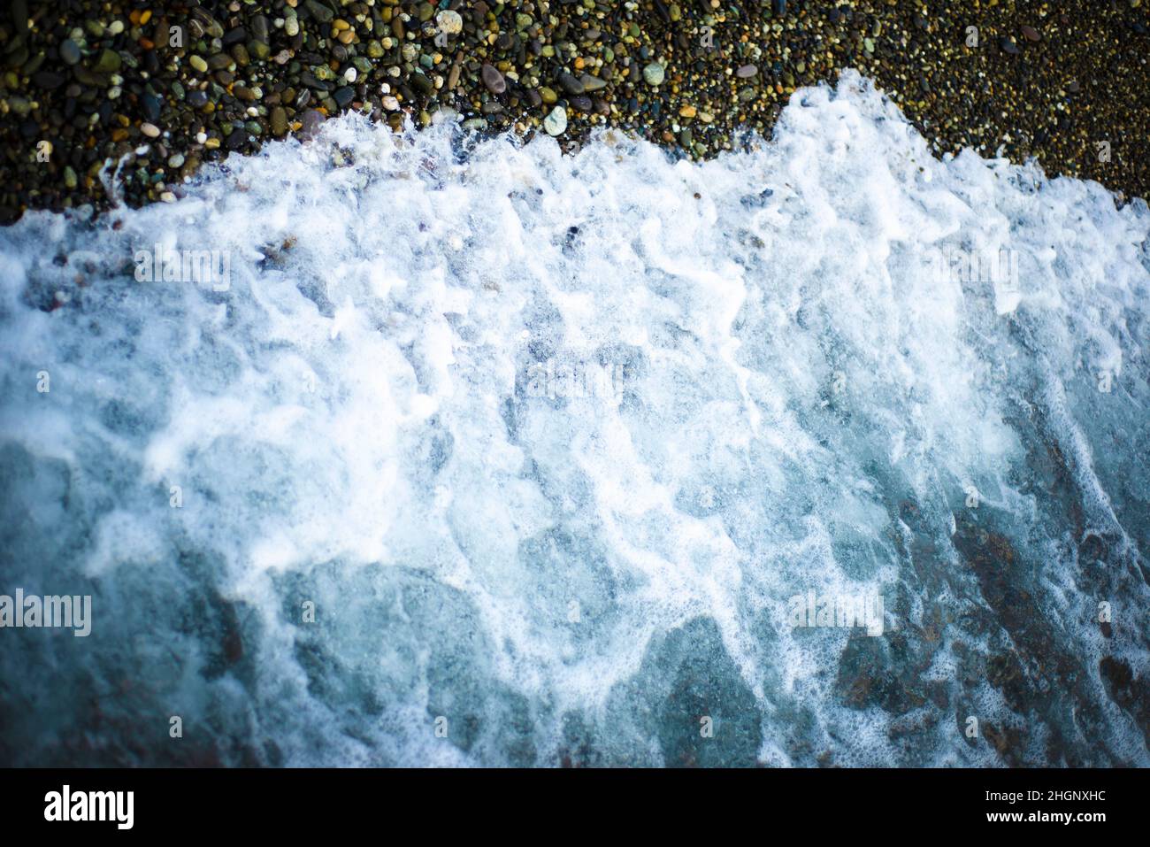 Schiuma di mare su una spiaggia di ciottoli. Primo piano. Strutture e sfondi marini. Foto Stock