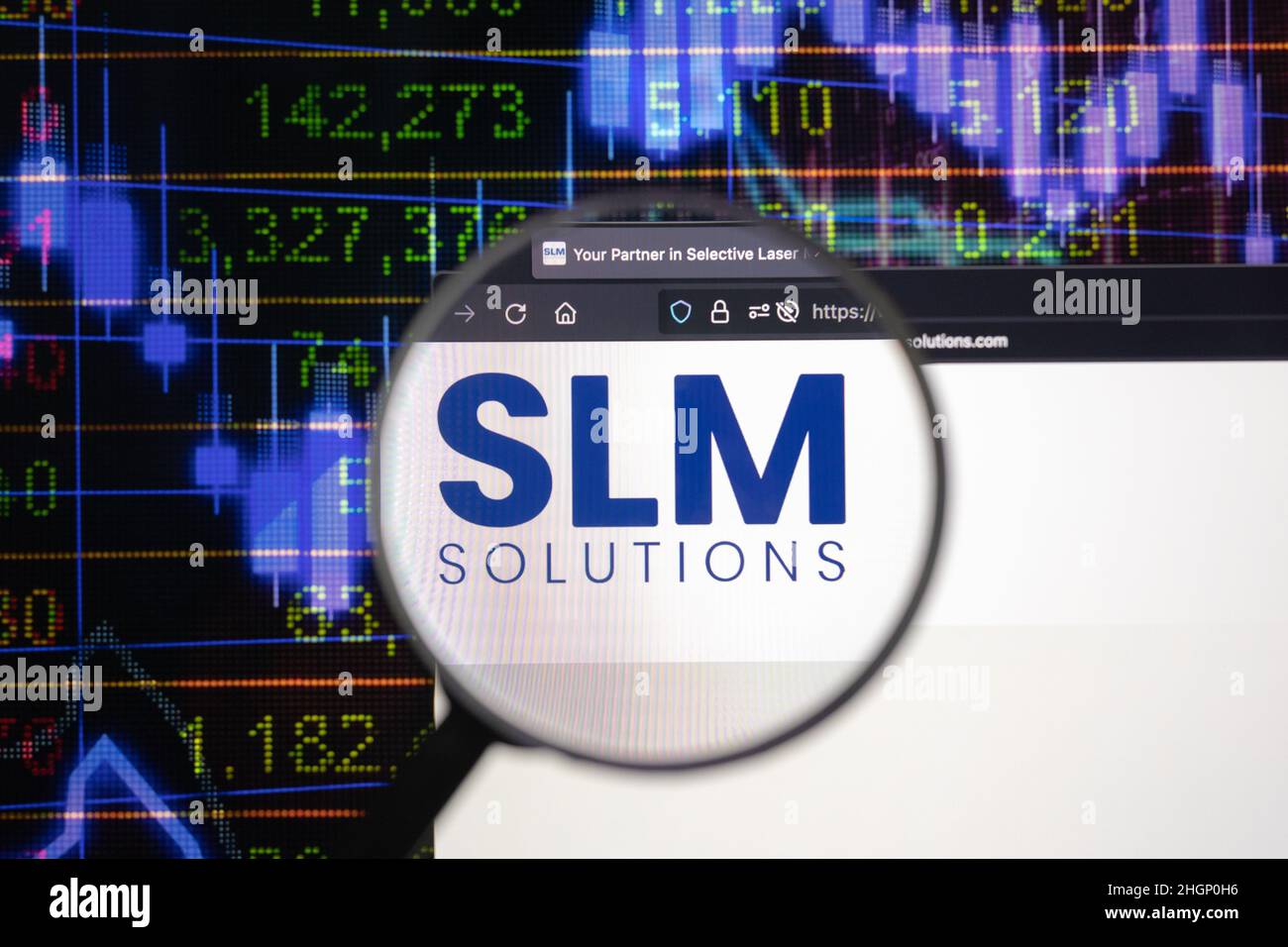 SLM Solutions logo azienda su un sito web con blurry sviluppi del mercato azionario in background, visto su uno schermo del computer attraverso una lente d'ingrandimento. Foto Stock