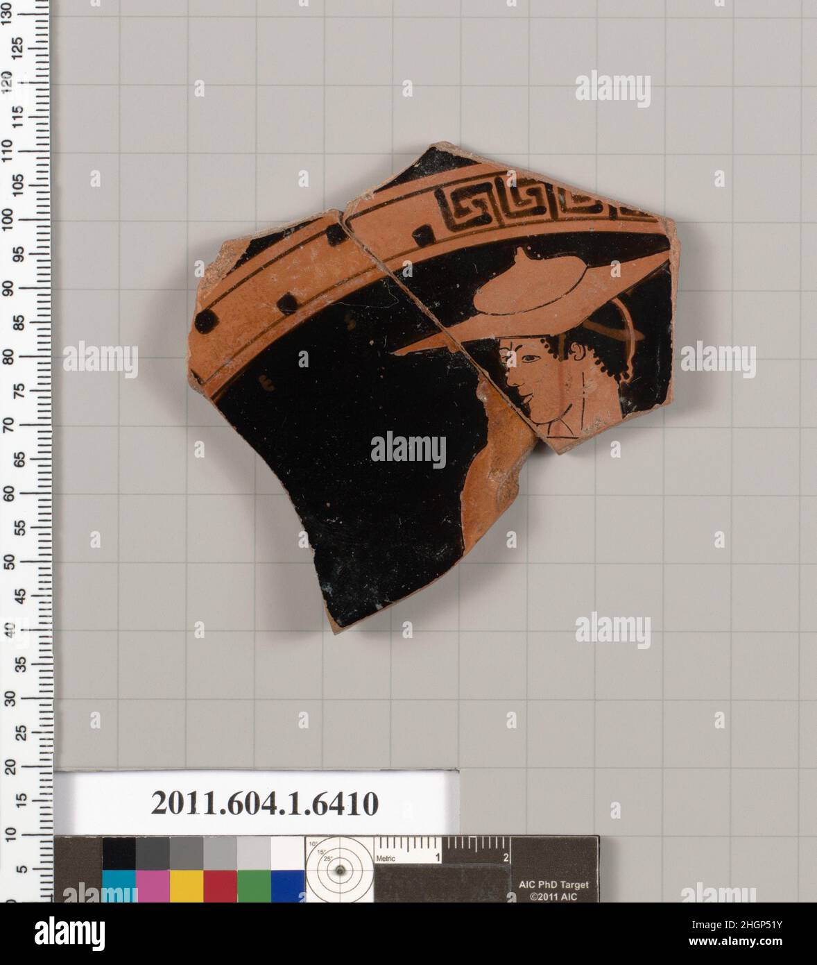 Frammento di terracotta di una kylix (tazza da bere) 490–480 a.C. Greco, Attico interno, testa, collo e spalla di giovani con filetto che indossa un petasos; dietro il ponte del naso, o occhio destro della giovinezza o occhio di un altro; due lettere di una iscrizione, ES. Frammento di terracotta di una kylix (tazza da bere) 709630 Foto Stock
