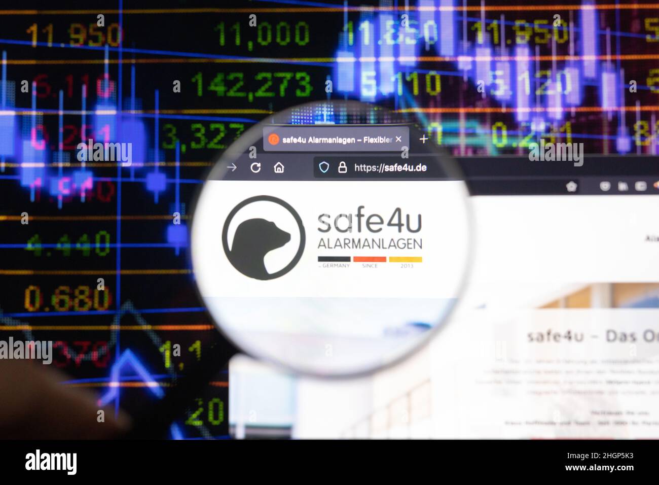 Safe4u logo aziendale su un sito web con sviluppi del mercato azionario sfocato in background, visto su uno schermo del computer attraverso una lente d'ingrandimento. Foto Stock