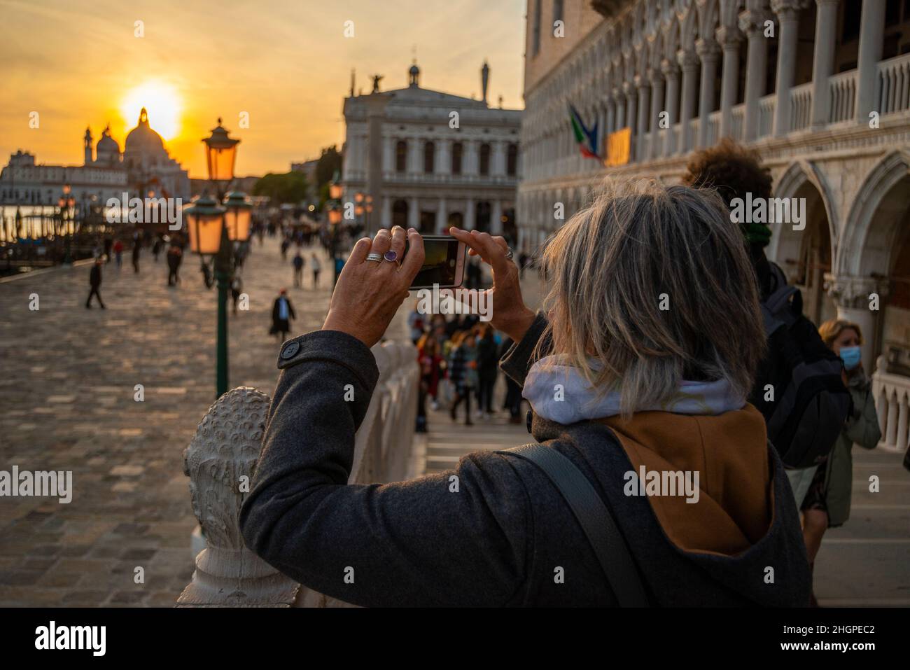 Donna con iPhone al tramonto con le lampade standard sulla Rive Shiavoni, il Canal Grande, Venezia, Italia Foto Stock