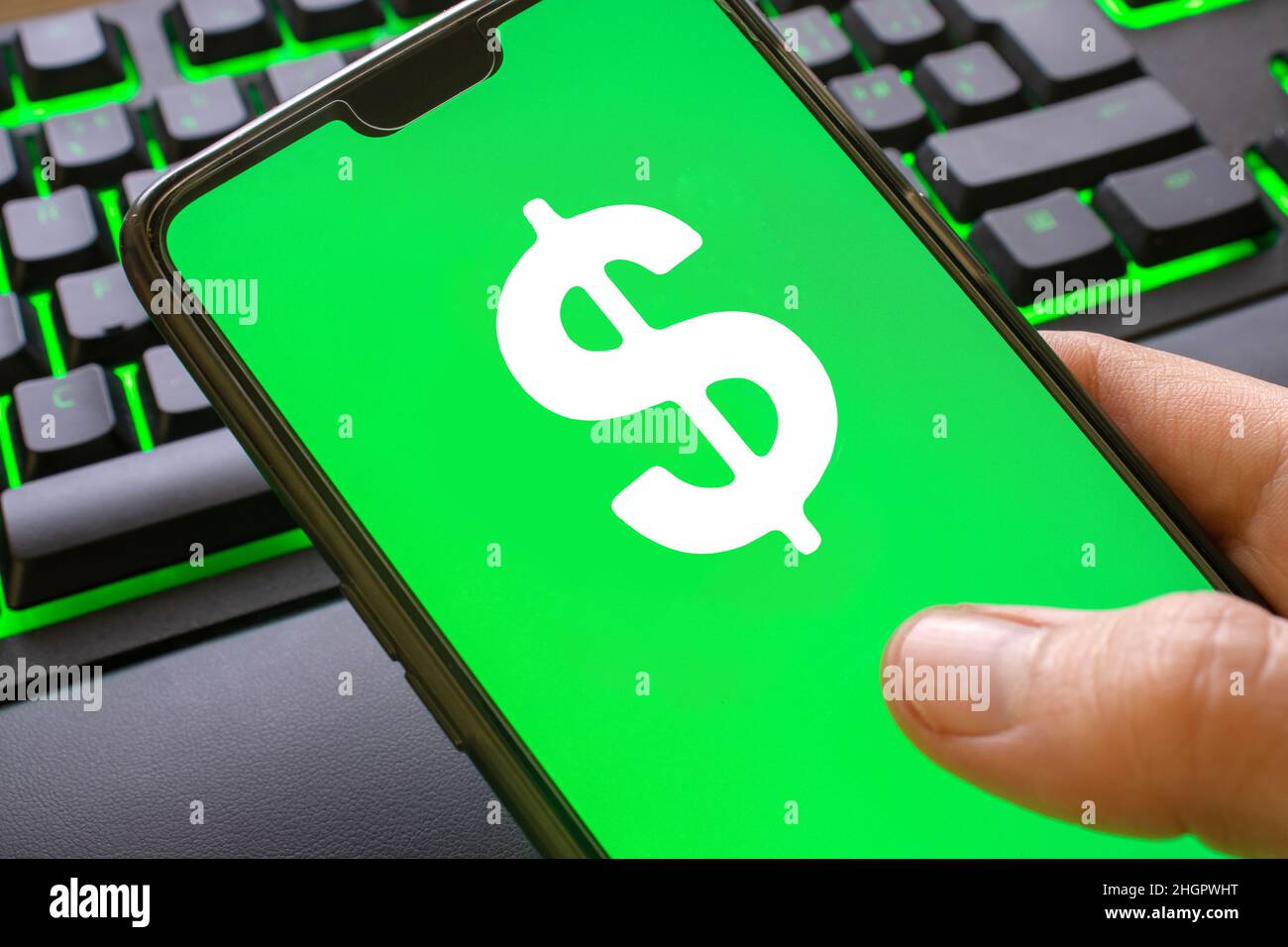 Telefono con simbolo verde del dollaro sullo schermo tenuto da una mano. Utilizzo dello smartphone per guadagnare denaro online con il logo della moneta. Foto Stock
