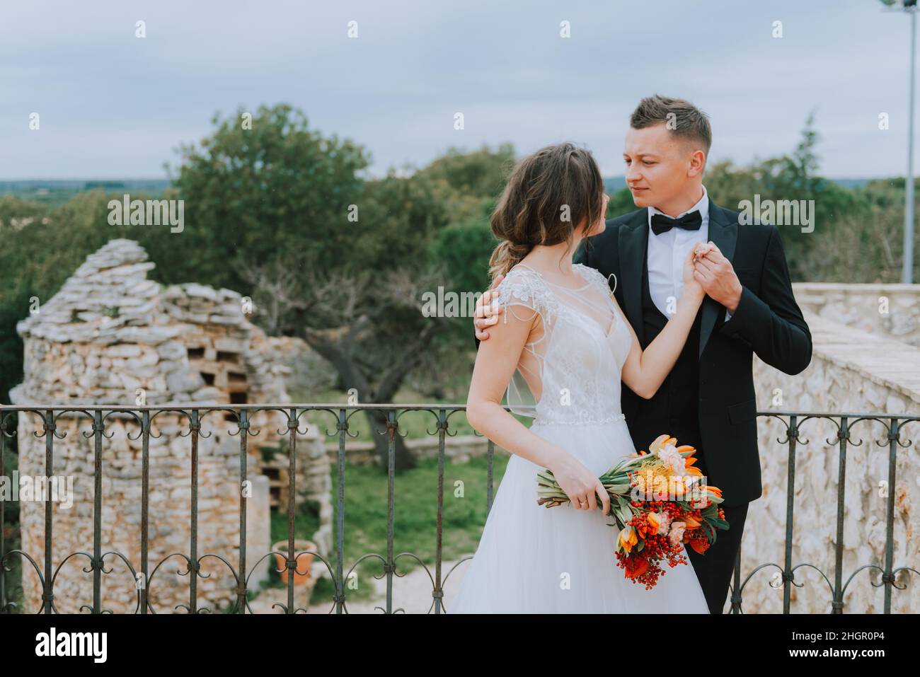 Felice coppia sorridente di stile che cammina in Toscana, Italia il giorno del matrimonio. La sposa e lo sposo camminano lungo la strada per le mani. Un giovane di stile Foto Stock