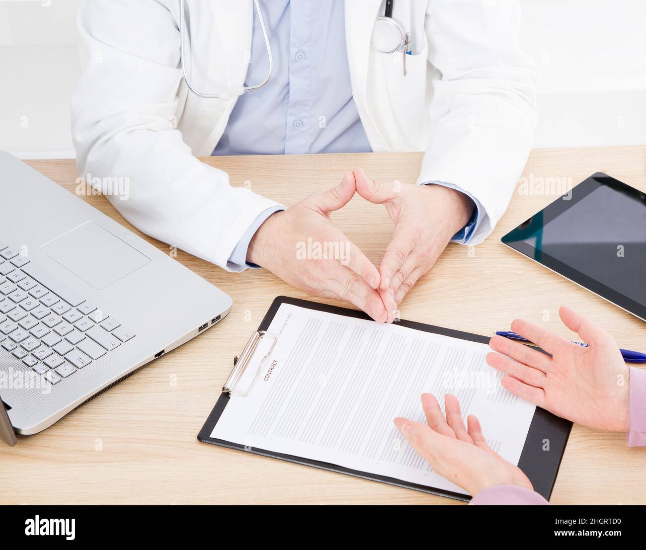 Medico e paziente stanno discutendo qualcosa, mani al tavolo. Assicurazione medica. DOC seduta nel mobiletto. Uomo in uniforme bianca. Foto Stock