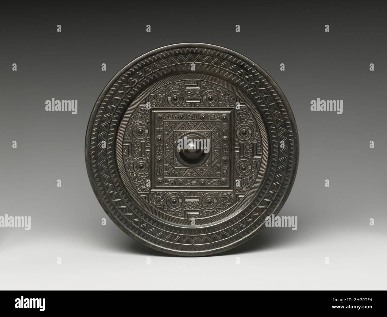 Specchio con design da gioco e animali delle quattro direzioni 1st–2nd secolo Cina la decorazione schematica sul retro di questo specchio punta a una nuova cosmologia. Il mondo quadrato, allineato con le quattro direzioni cardinali e inscritto con i “dodici rami terreni” usati per calcolare il calendario, è circondato dai cieli circolari, a loro volta inanchiati dalle onde dell’oceano cosmico. Condividere il regno celeste con gli animali delle quattro direzioni sono segni a forma di T, L e V che richiamano lo stesso disegno sul tabellone di gioco di liubo, suggerendo che un gioco d'azzardo gioca anche un ruolo in Foto Stock