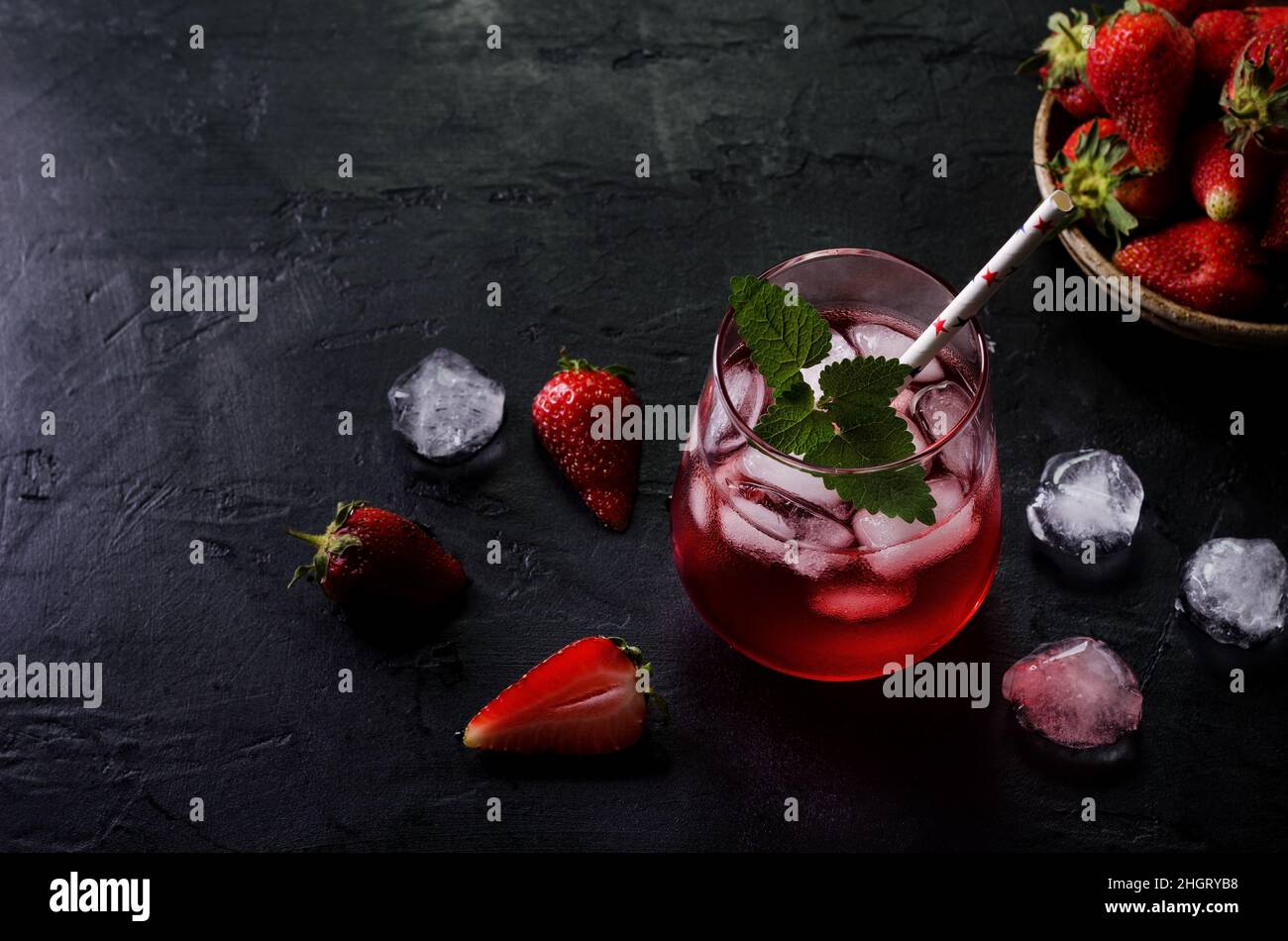 Cocktail freddo con fragole e ghiaccio su sfondo nero. Bevande estive in modo scuro. Foto Stock