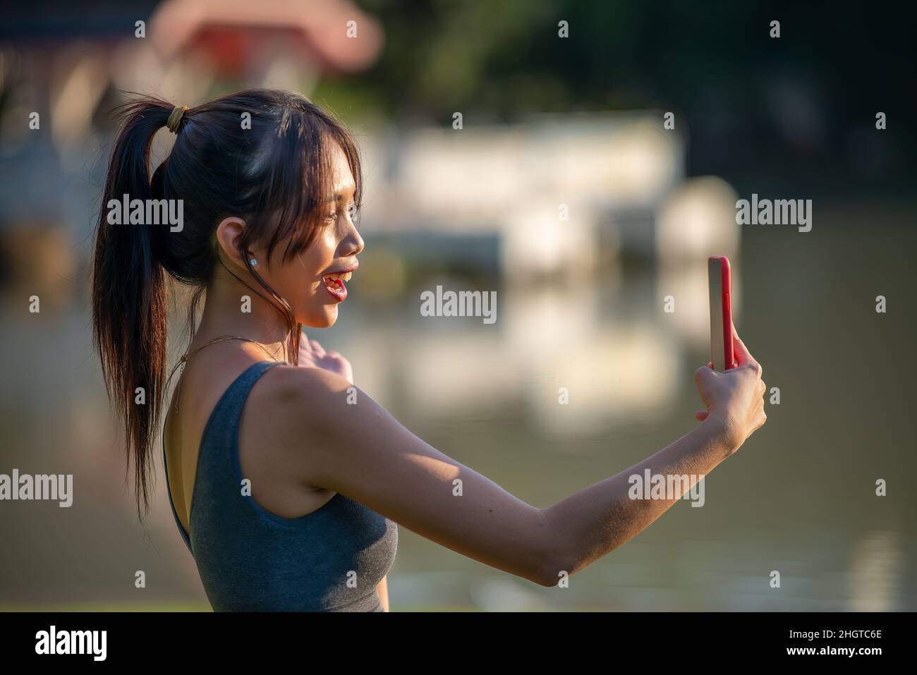 Giovane e bella donna asiatica che si esercita nel parco della città, utilizzando il suo smartphone per catturare i momenti di fitness Foto Stock